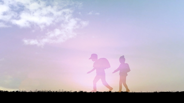 夕焼け空の中を歩く2人の子どもの影