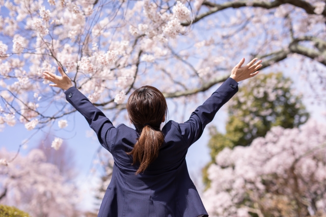 桜を見上げて万歳をする女性学生の後ろ姿