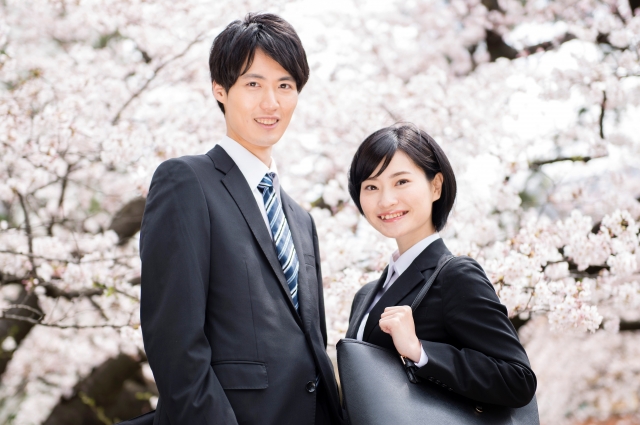 桜を背景に立つスーツ姿の若い男女